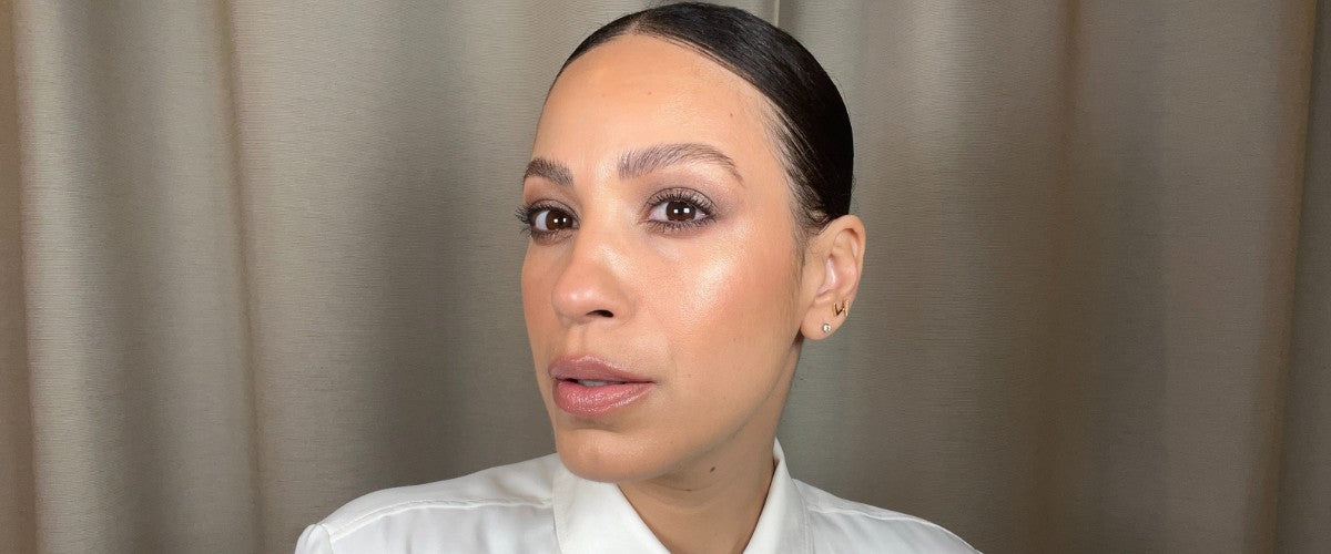 Close-up of a woman with slicked-back hair wearing classic natural makeup: neutral eyeshadow, subtle highlight, nude lip.