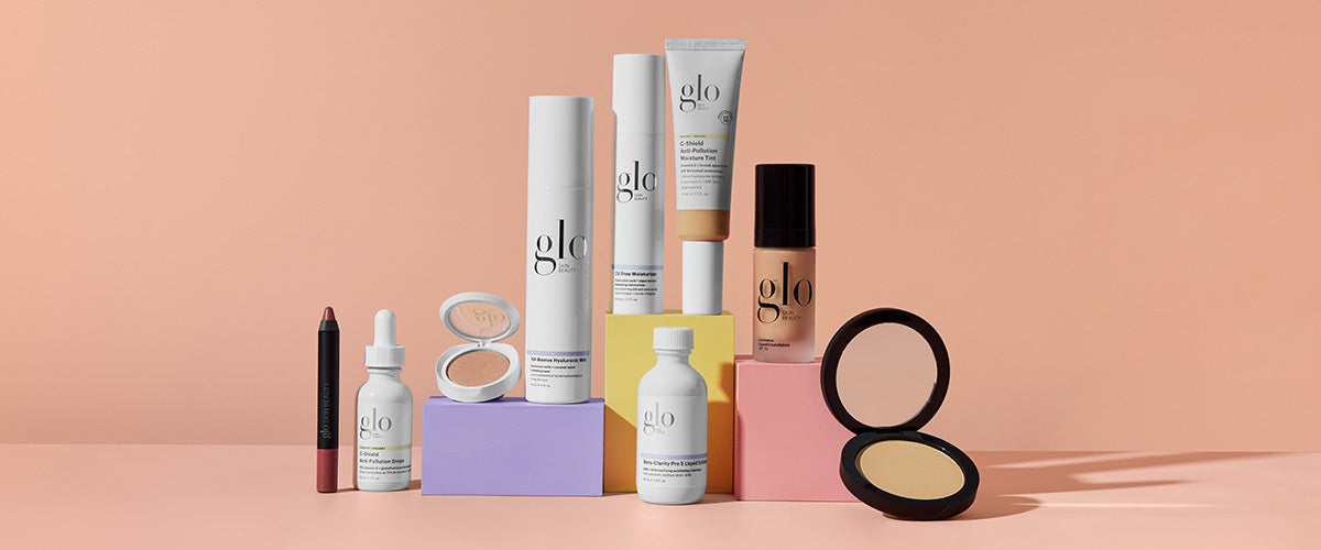 Assorted glo skincare and makeup products (serum, foundation, powder, lip crayon) on pastel blocks with peach background