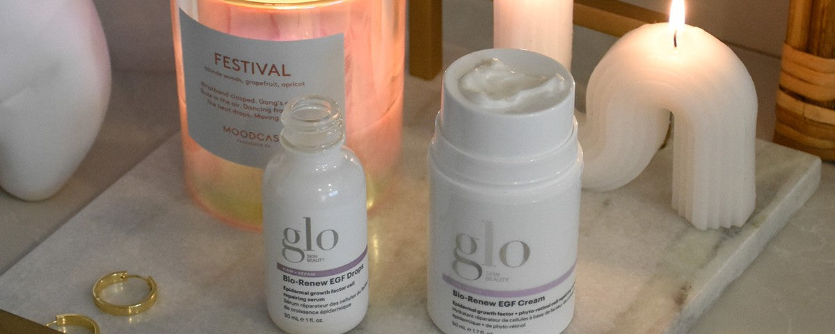 Two glo SKIN BEAUTY products labeled 'Bio-Renew EGF Drops' and 'Bio-Renew EGF Cream' on a marble tray with FESTIVAL MOODCASE candle.