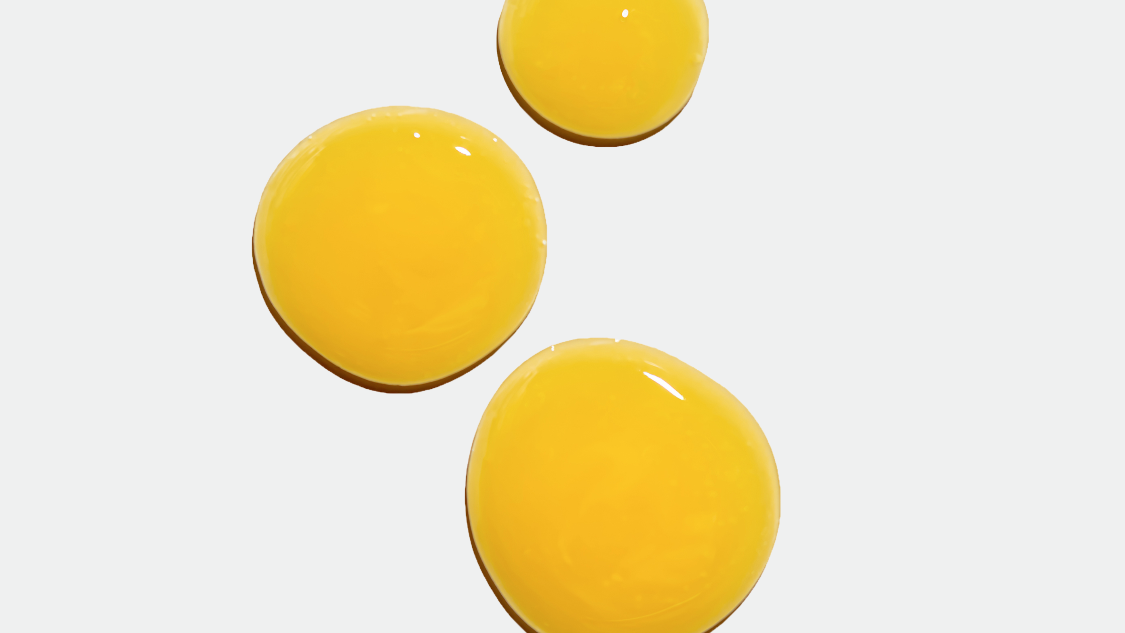 Three glossy yellow serum drops on a pale background, varying sizes with soft highlights.