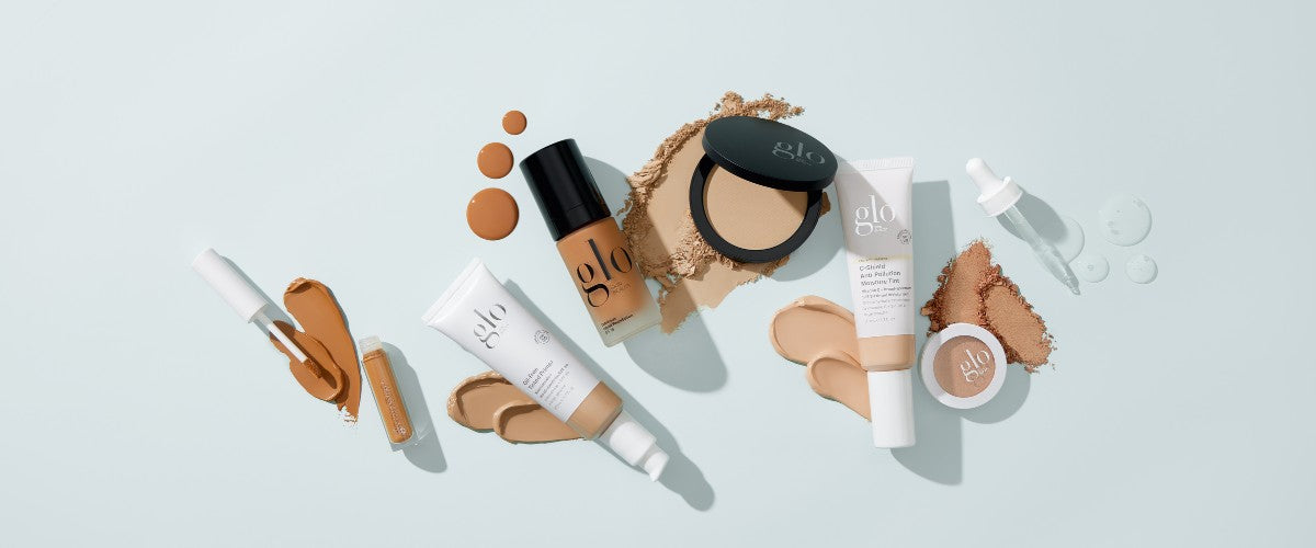 Assortment of foundation bottles, tubes, compact, powders and swatches on pale blue background; visible branding: 'glo'.