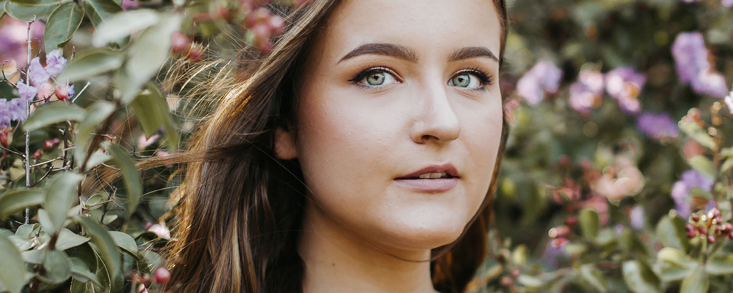 Young woman among flowering bushes, close-up of her face with subtle flushed cheeks, looking slightly off-camera