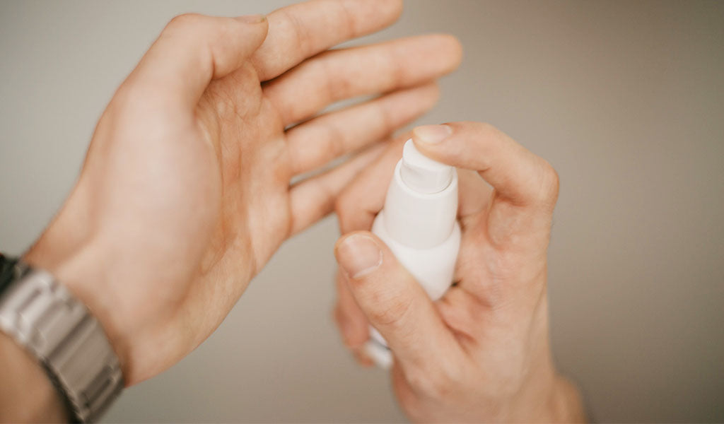 Hands holding a white pump bottle dispensing skincare serum onto palm