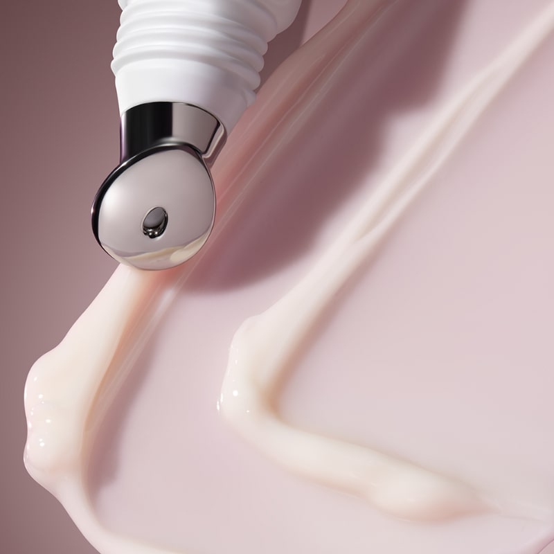 Metal-tipped cosmetic applicator touching swirls of pale-pink skincare cream on a smooth surface