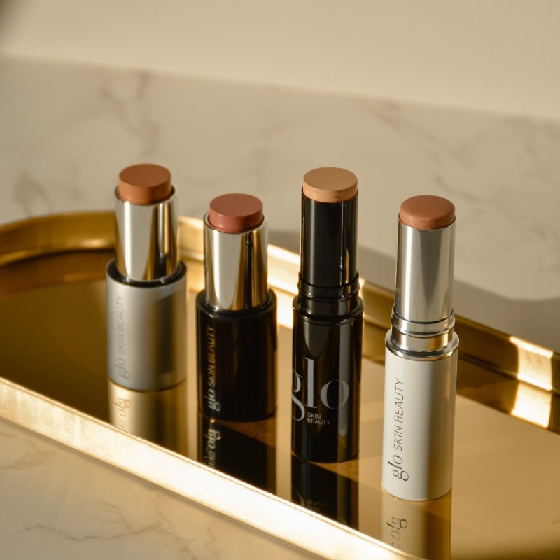 Four cream contour and highlight sticks on a gold tray, brand text glo SKIN BEAUTY visible.