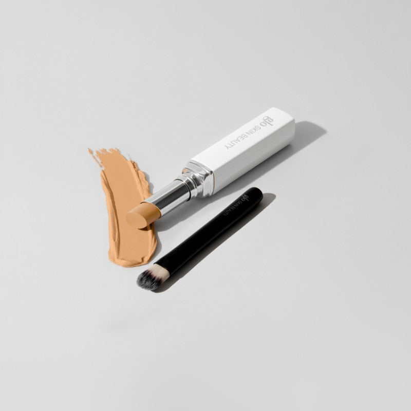 Concealer stick with beige smear and short brush; packaging label reads "SKIN BEAUTY".