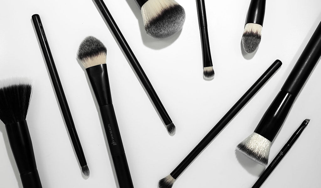 assorted black-handled makeup brushes with white-tipped bristles arranged on a white background