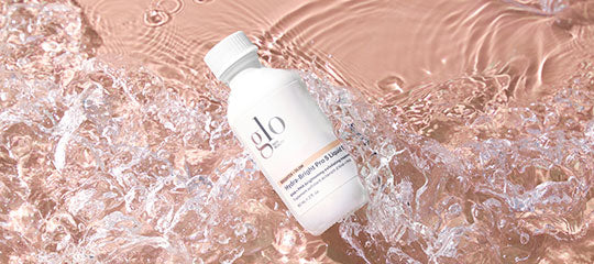 white 'glo' skincare bottle lying on rippling pink water