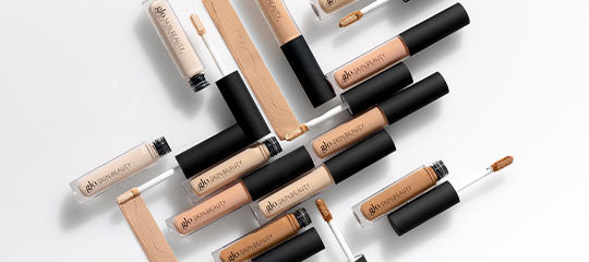 Multiple concealer tubes and applicators arranged diagonally with swatches showing a range of skin tones