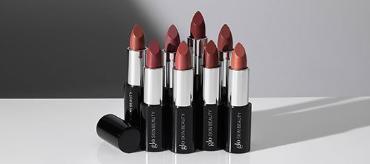 Seven lipsticks by glo skin BEAUTY in assorted mauve and red shades, caps removed; one cap on its side.