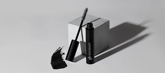 Mascara tube and wand with mascara smudge on surface, glo SKIN BEAUTY branding on tube