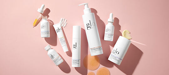 Flat-lay arrangement of white glo skincare bottles, pump and dropper on pink background with cotton swabs and round pads.