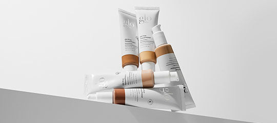 Five glo skincare tubes in varying tan shades stacked on a white ledge, showcasing foundation/cream packaging