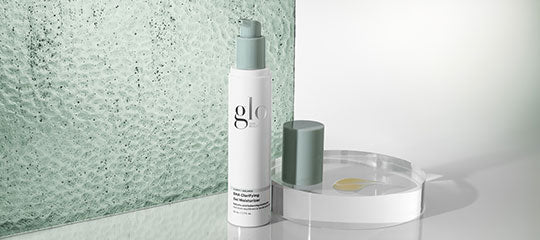 glo pump bottle with green cap beside a shallow clear dish on a reflective surface with textured green glass backdrop