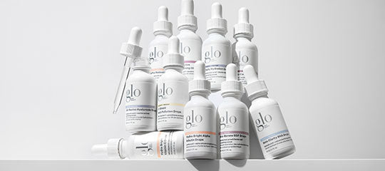 White dropper bottles labeled 'glo' arranged in a stacked group on a white surface