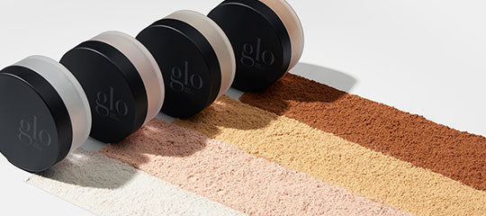 Four black glo compacts on five textured powder swatches ranging from ivory to deep brown