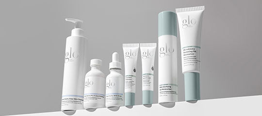 Row of white and pale-green glo skincare bottles and tubes arranged on a ledge.