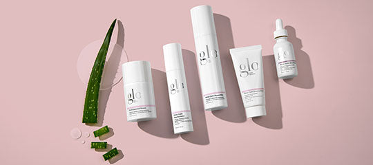 glo skincare bottles and serum with an aloe leaf and sliced aloe on a pink background
