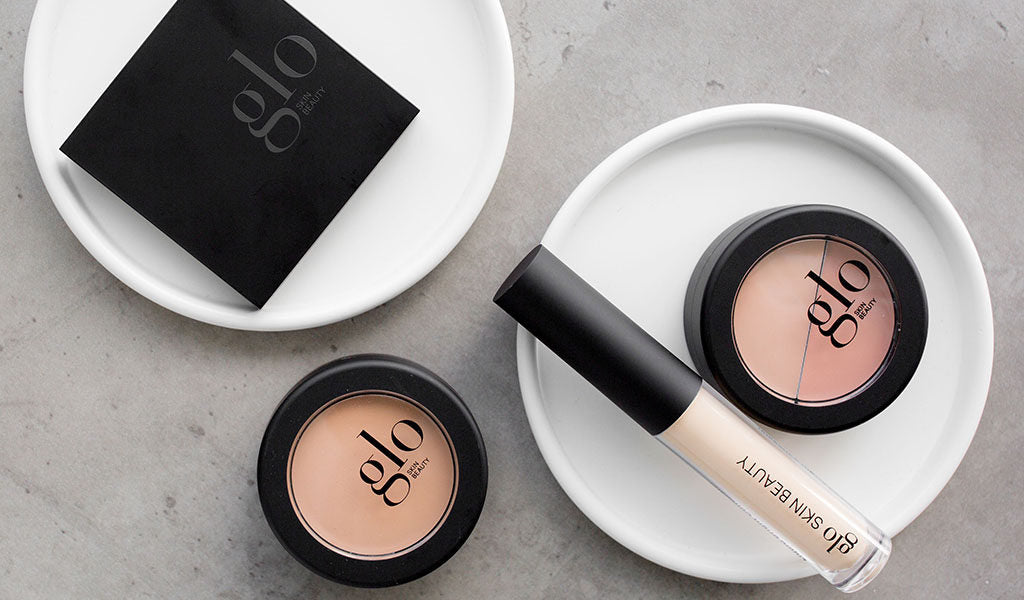 Three concealer compacts and a tube labeled glo SKIN BEAUTY, arranged on white dishes