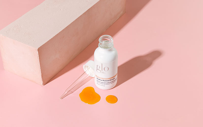 glo bottle labeled GlyPro Retinol Drops with pipette and orange serum spills on pink background