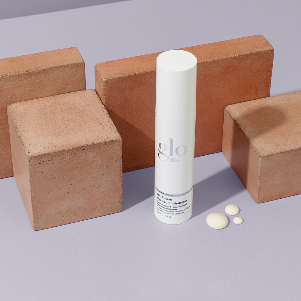 glo SKIN BEAUTY HA-Revive Hyaluronic Hydrator bottle with three cream drops beside terracotta blocks