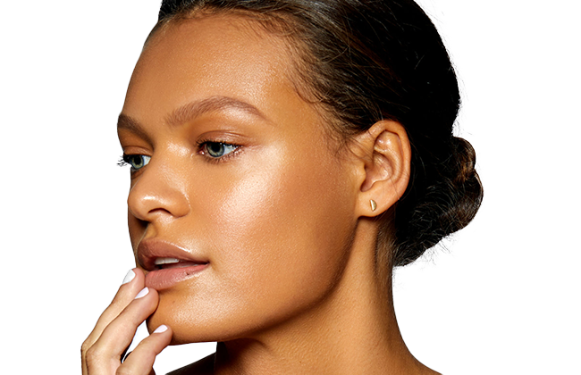 Close-up portrait of a woman with glowing skin, hand at her chin and a small gold earring.