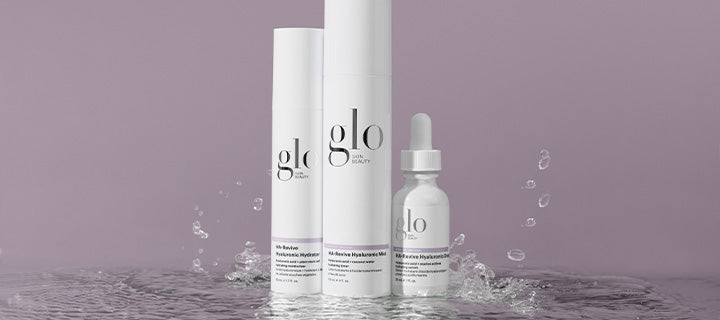 Three glo skincare products — two pump bottles and one dropper bottle with water splashing on a mauve background