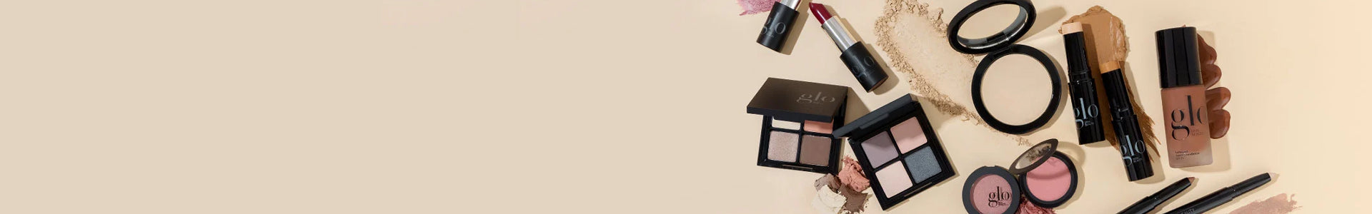 Assorted glo makeup on beige background: eyeshadow palettes, compact, blush, foundation bottle, lipsticks and pencils.