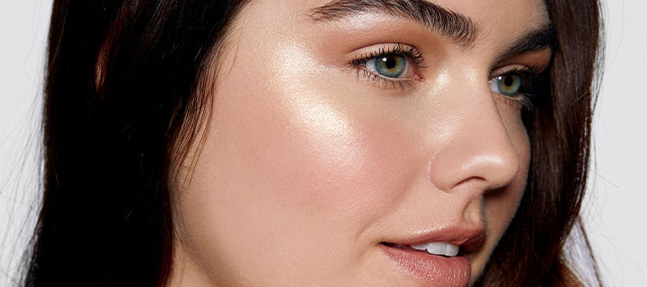 Close-up portrait showing dewy makeup on a woman's cheekbone and green eyes
