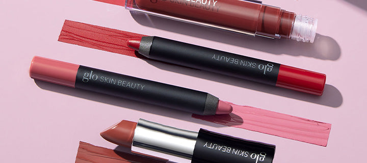 Three lip crayons and a lipstick with color swatches, branded glo SKIN BEAUTY, on a pink background