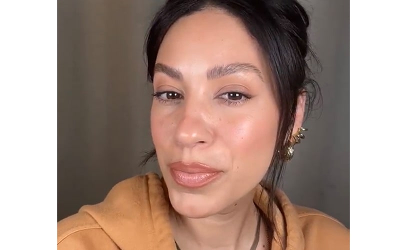 Close-up of a woman wearing nude lipstick, warm-toned makeup, and a gold ear cuff.