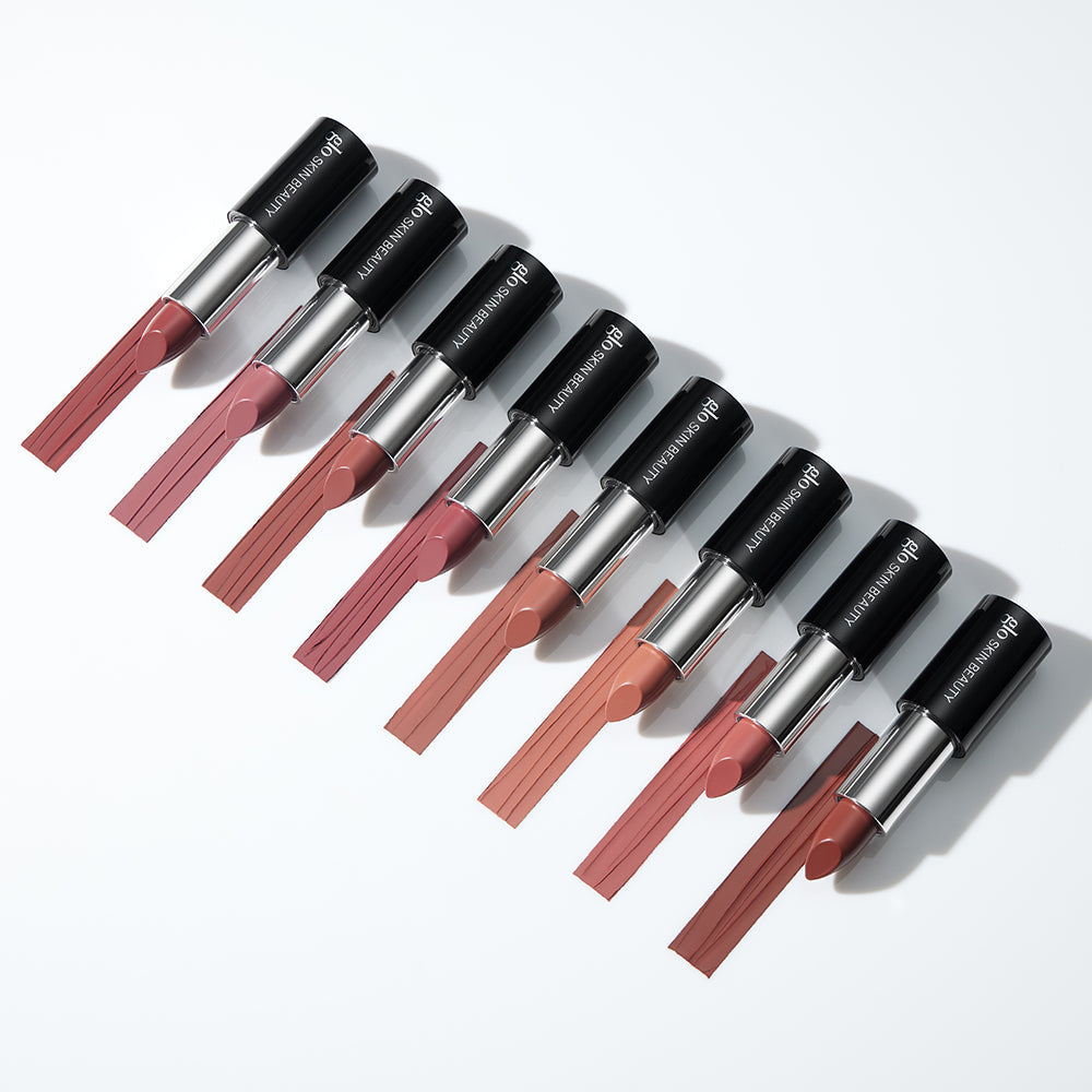 Nine satin lipsticks in neutral shades arranged diagonally, caps labeled glo SKIN BEAUTY