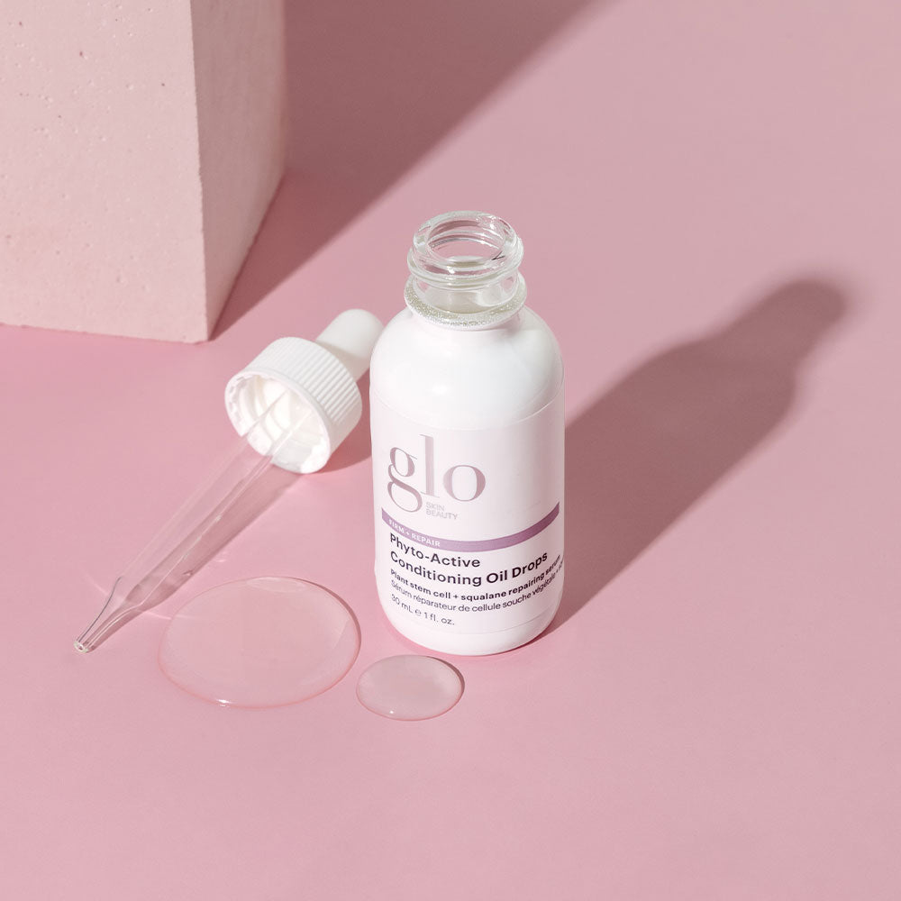 glo skin beauty Phyto-Active Conditioning Oil Drops bottle, dropper, and oil puddles on pink background — 30 mL e 1 fl. oz.
