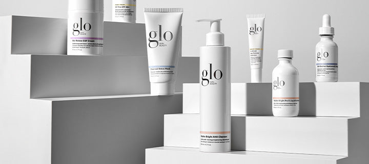 Assorted white glo skincare bottles and tubes arranged on stepped white blocks, minimal studio display
