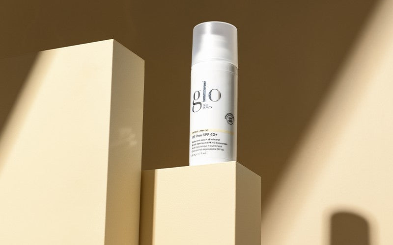 glo skin beauty bottle labeled Oil Free SPF 40+ on beige pedestal with strong sunlight and shadows