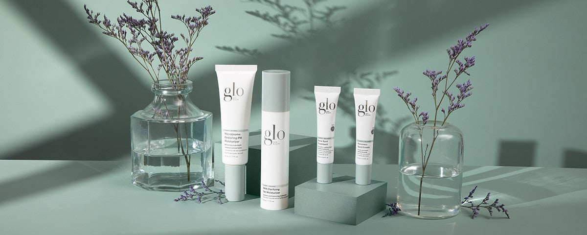 glo skincare tubes and bottle with glass vases and lavender sprigs on mint-green background