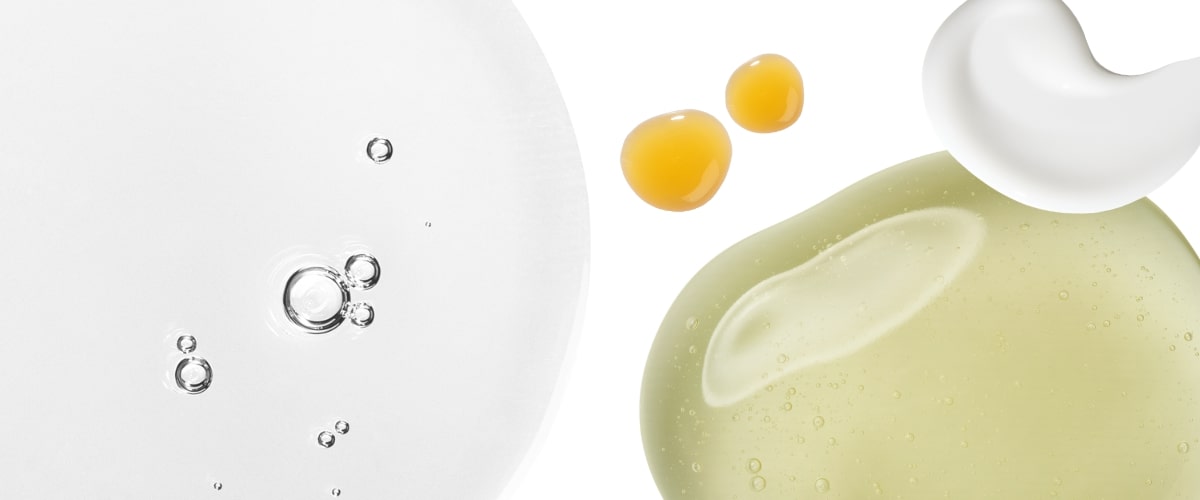 Close-up droplets and swirls of clear gel, yellow oil, and white cream on a white background