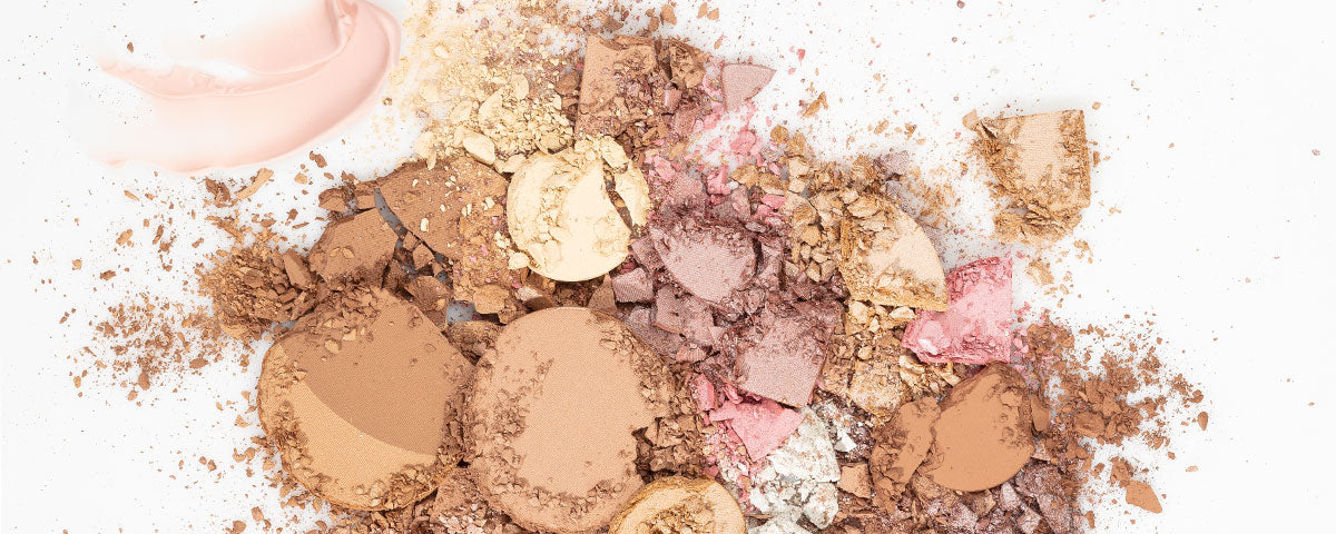 Assorted crushed blush makeup: broken powder pans and a pale pink cream smear on white background.
