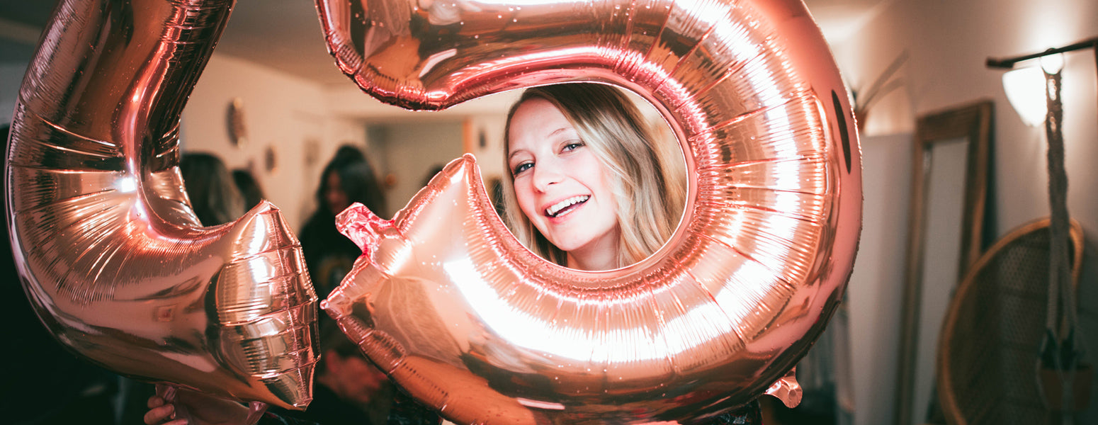 Smiling woman framed inside a rose-gold number 5 foil balloon at a party
