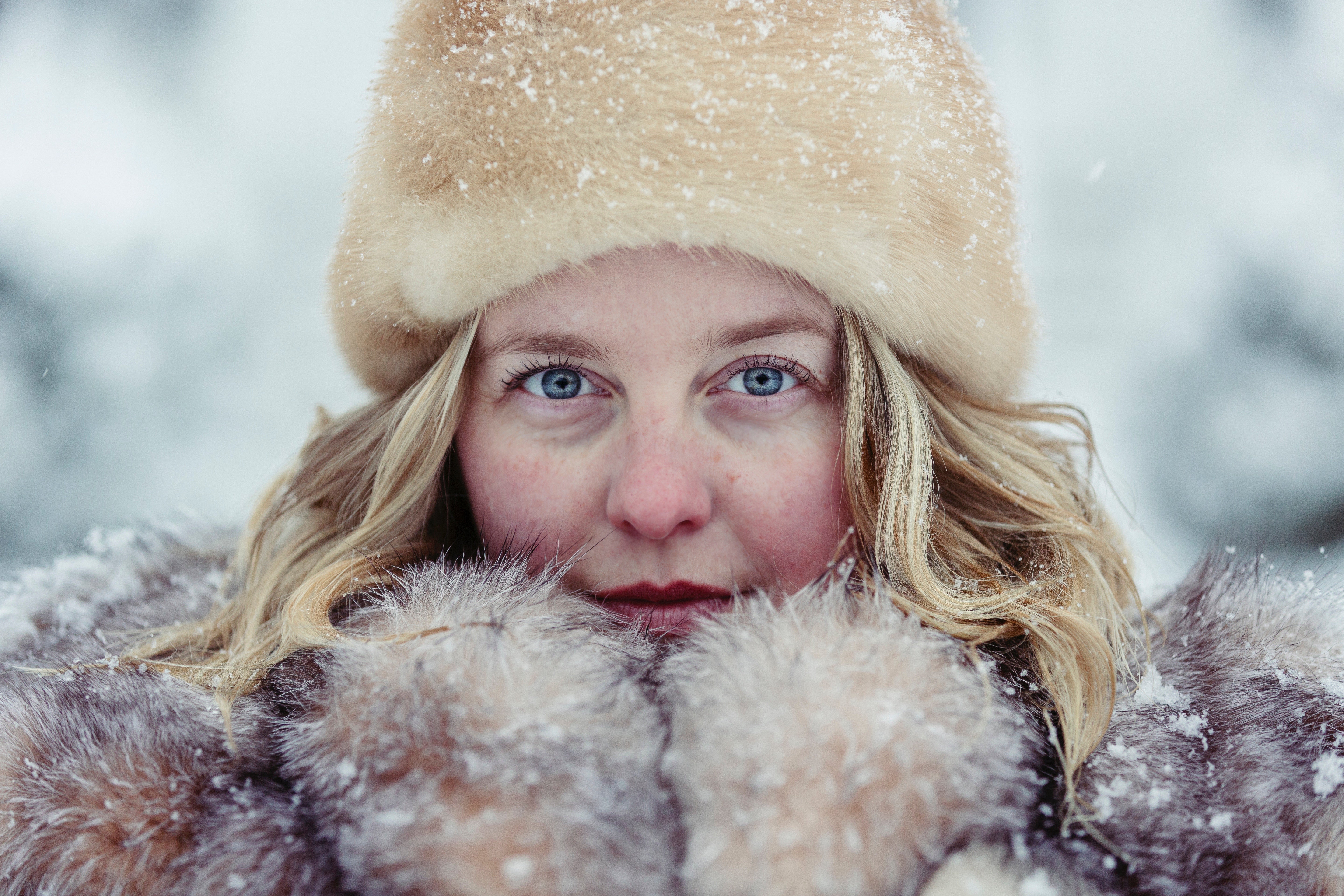 Blue-eyed woman wearing a fur hat and snow-dusted coat, cheeks flushed from the cold