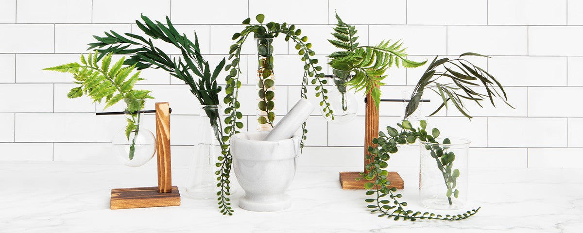 Mortar and pestle with vining plant cuttings and glass vials on a white tiled counter