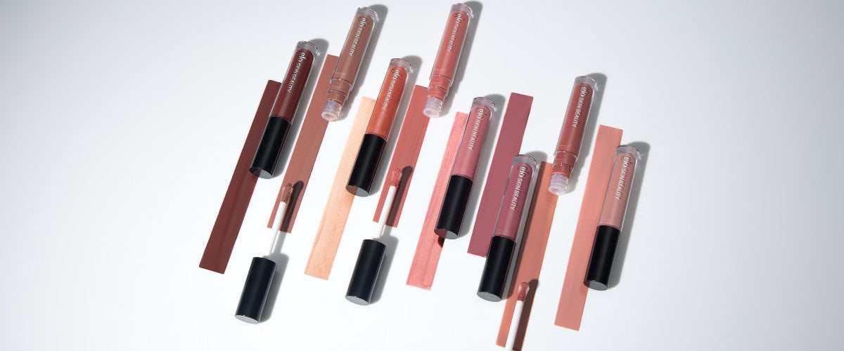 Multiple lip-gloss tubes with wands and painted color swatches in mauve, peach, and nude shades