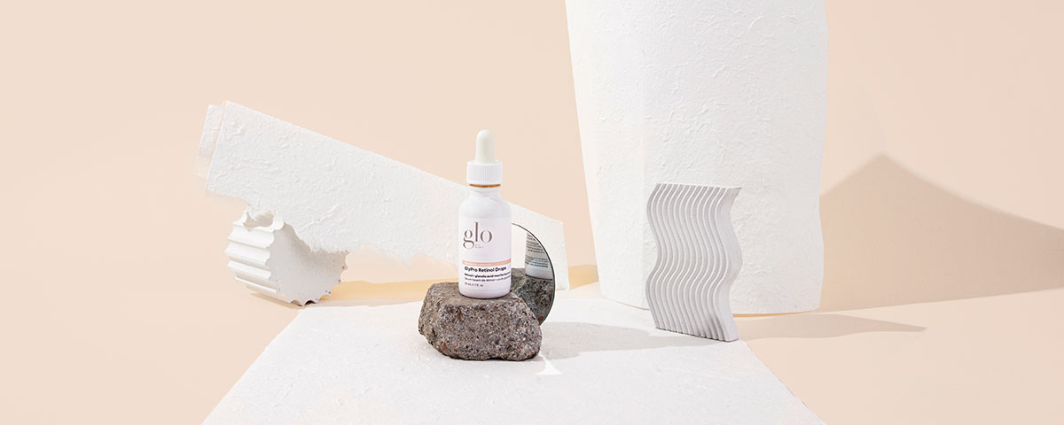 glo serum bottle on a rock amid white sculptural props against a pale beige background