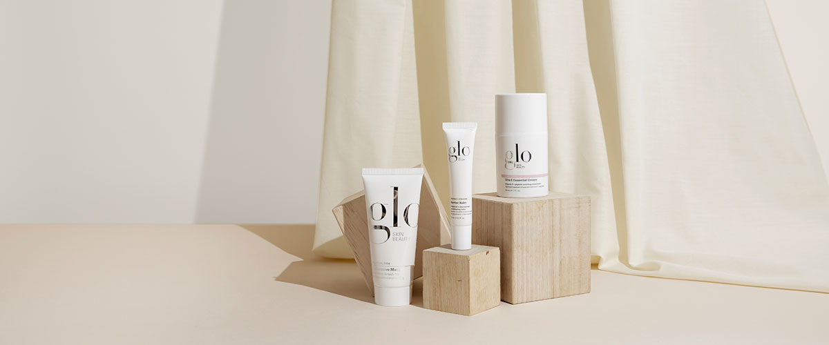 Three glo SKIN BEAUTY skincare products (tube, squeeze tube, jar) on wooden blocks against a cream backdrop.
