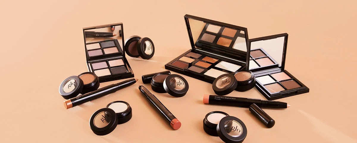 Assorted glo eyeshadow palettes, cream shadow pots and eye-shadow sticks arranged on a beige background