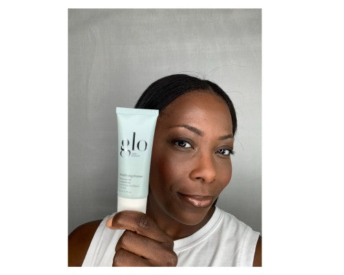 Woman holding a tube labeled 'glo' beside her face, showing skin finish