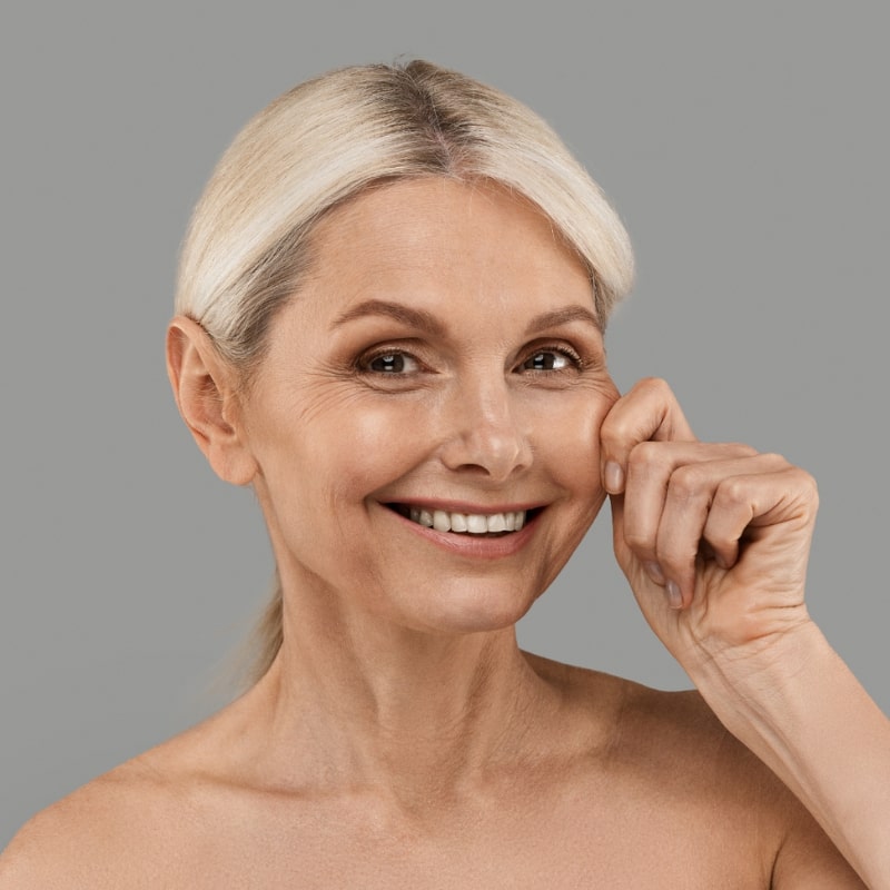 Smiling older woman lightly pinching her cheek to show skin firmness
