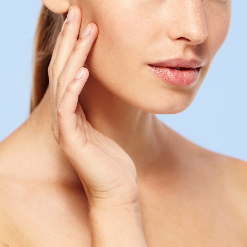 Close-up of a person's lower face as fingertips gently pull the cheek