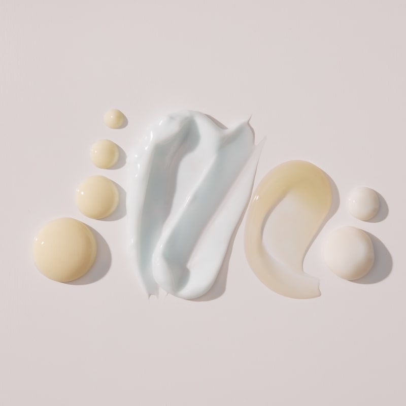 Three skincare product swatches on pale background: white and pale-blue cream smears plus beige translucent lotion drops.