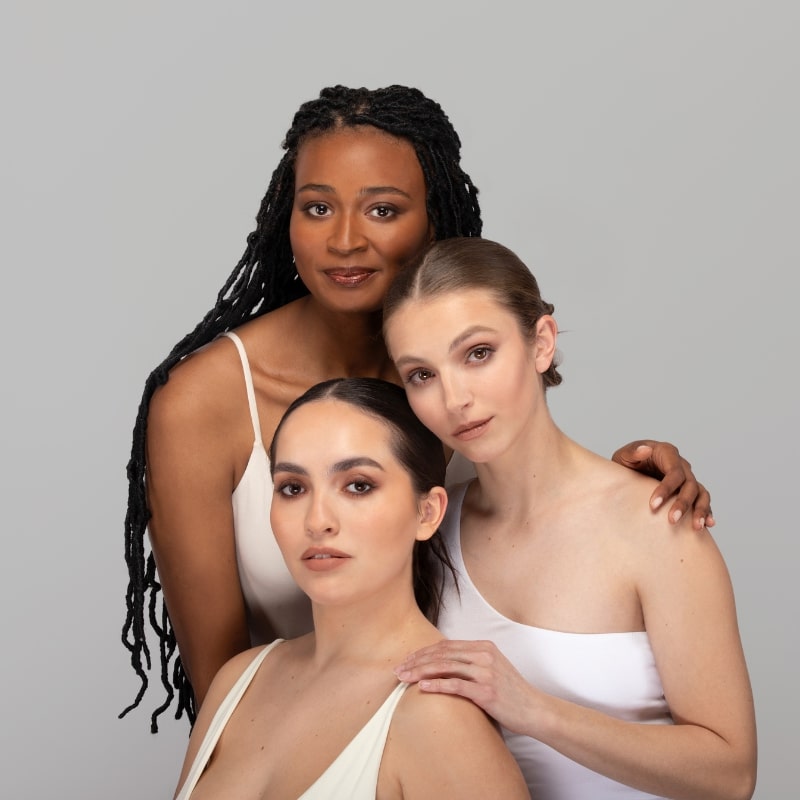 Three women with contoured makeup posing closely against a neutral gray background